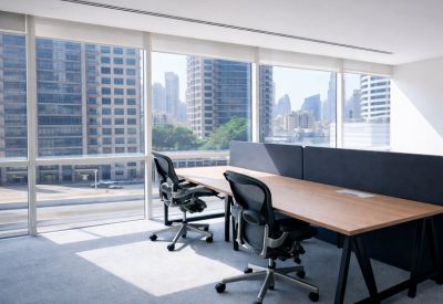 Bright private office featuring a wooden desk, black ergonomic chairs, and floor-to-ceiling city views.