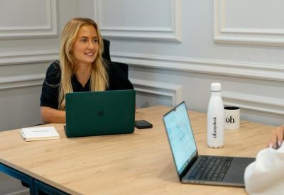 A woman working at a wooden desk with a green laptop.