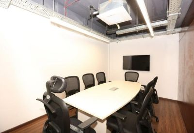 Modern conference room with a light wood table and wall-mounted screen.