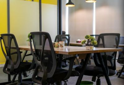 Long wooden communal table surrounded by black mesh chairs under bright yellow accents.