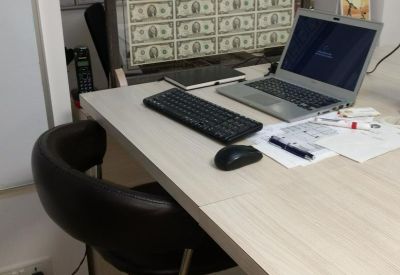 Modern workspace featuring a laptop on a light wood desk next to a unique glass-encased currency display.