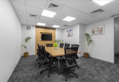 Professional meeting room with a wooden table, wall-mounted screen, and potted plants.