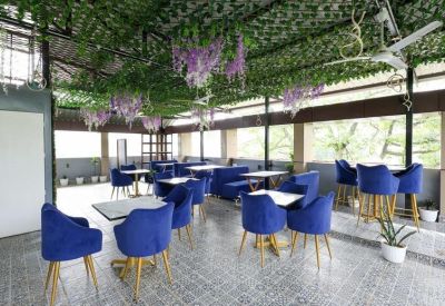 Vibrant rooftop cafe area with blue velvet seating under a ceiling covered in artificial greenery and flowers.