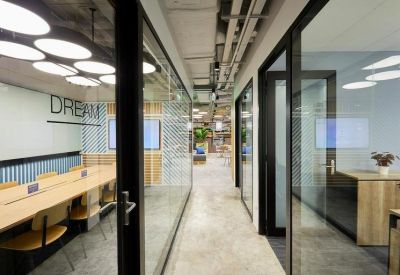Bright office corridor featuring glass-walled suites and wooden accents.
