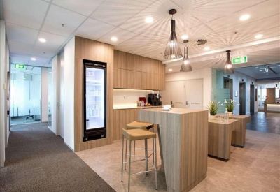 Modern communal kitchen and breakout area with wooden cabinetry and bar stool seating.