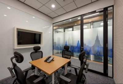 Small meeting room with four mesh chairs around a light wood table and wall-mounted screen.