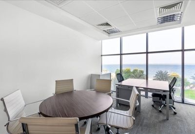 Bright corner office with meeting table, desk, and sea views through floor-to-ceiling windows.
