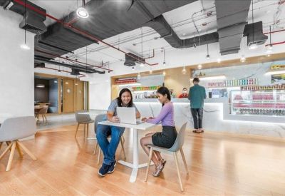 Vibrant communal lounge with wooden floors, industrial ceilings, and people working at tables.