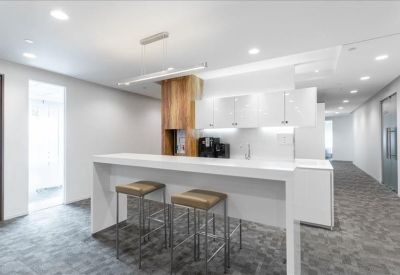 Modern communal kitchen and breakout area with a white breakfast bar and wooden stools.