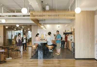 Communal kitchen and breakout area with wooden floors and people socialising near a breakfast bar.