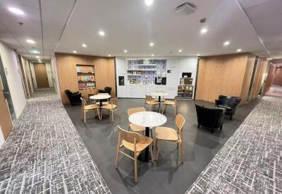 Spacious communal breakout area with cafe tables and a kitchen service point in the background.