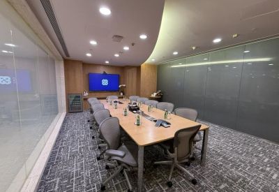 Formal boardroom featuring a long wooden table, ergonomic chairs, and a wall-mounted display screen.