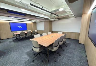 Spacious boardroom with a large wooden table, grey chairs, and a large wall-mounted monitor.