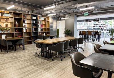 Bright communal lounge and coworking area with long wooden tables and floor-to-ceiling bookshelves.