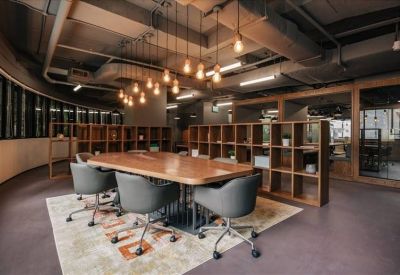 Warm meeting space with a large wooden table, grey armchairs, and hanging filament bulb lighting.