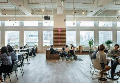 Sunlit open-plan coworking space with large windows overlooking the city.