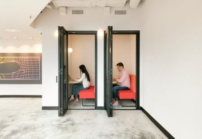 Two private soundproof phone booths with red seating in a minimalist corridor.