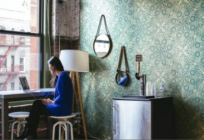 Workspace by a window with a patterned feature wall and a person using a laptop.