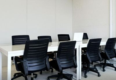 Shared workspace area with multiple white desks and black mesh office chairs.