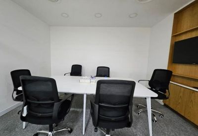 Minimalist meeting room with a clean white table, black mesh chairs, and a wall-mounted screen.