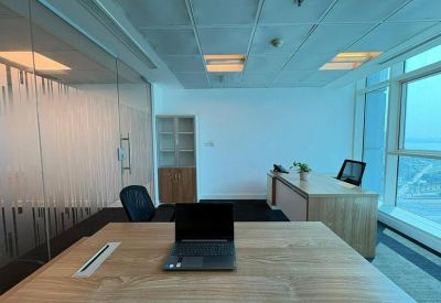 Private office featuring a large wooden desk with a laptop and view of a glass partition.