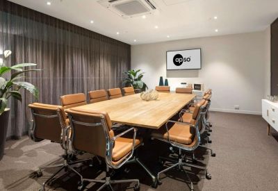Formal boardroom featuring a long wooden table, tan leather chairs, and a wall-mounted screen.