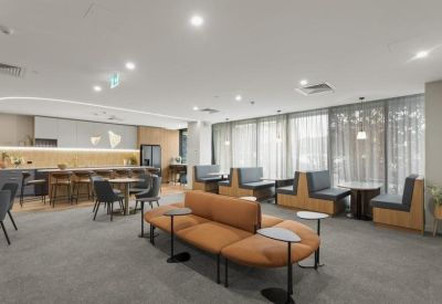 Expansive breakout lounge with tan sofas, booth seating, and a modern kitchen in the background.