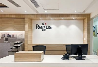 Bright reception desk area with a large Regus brand logo on a wood-paneled wall.