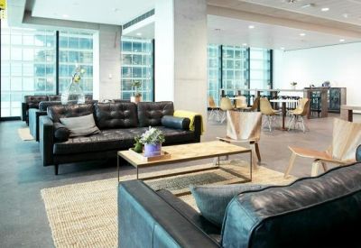 Modern communal lounge with black leather sofas, wooden coffee tables, and a bright coworking space.