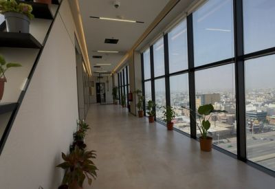 Luminous hallway at Custodian of The Two Holy Mosques Road with floor-to-ceiling windows and potted plants.