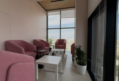 Sunlit lounge area with pink armchairs and white coffee tables next to a large window.