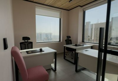 Bright private office featuring three white desks, ergonomic chairs, and large windows with city views.