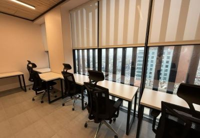 Bright coworking space with long desks facing large windows with striped blinds.