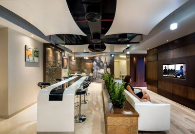 Modern breakroom featuring a high white breakfast bar and a lounge area with a wall-mounted TV.