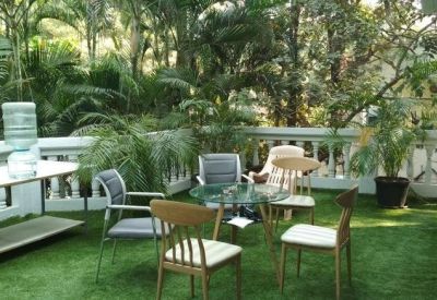 Outdoor terrace lounge with artificial grass, patio furniture, and lush green trees.