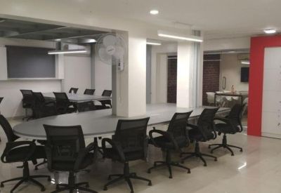 Spacious open-plan office with a long grey conference table and black mesh chairs.