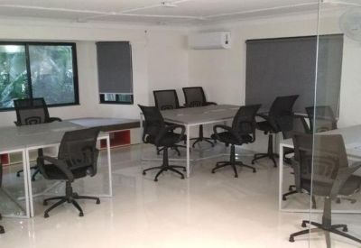Well-lit coworking space with multiple white desks and ergonomic black chairs.