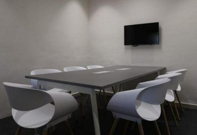 Minimalist meeting room with a dark grey table, white chairs, and a wall-mounted TV.