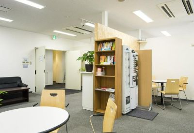 Communal breakout space with round tables, light wood chairs, and a refreshment area.