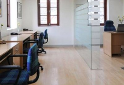 Spacious open-plan office with light wood desks and blue ergonomic chairs.