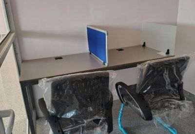 Close-up of a two-person workstation with a blue privacy divider and blue-framed chairs.