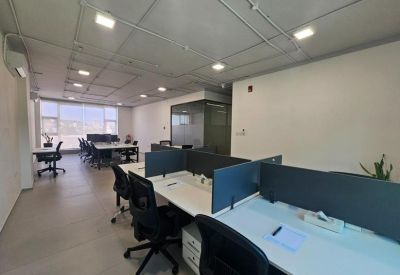 Open-plan office space with rows of white desks and black ergonomic chairs.