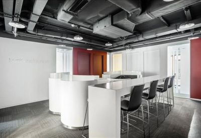 Modern breakout area with white curved counters, high stools, and industrial exposed ceilings.