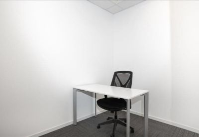Private windowless office suite with a white desk and black ergonomic chair.