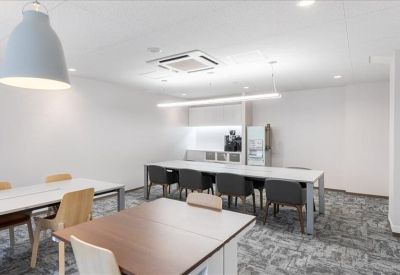 Communal breakout area featuring long white tables, a coffee station, and grey carpet.