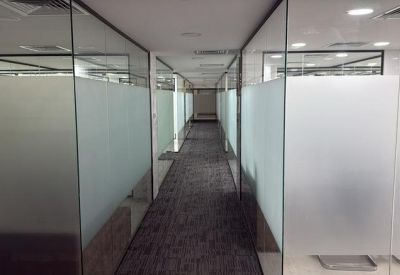 Bright hallway lined with glass-walled office suites and frosted privacy panels.