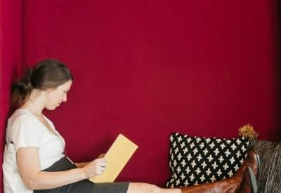 Woman reading in a private red acoustic seating nook with decorative pillows.