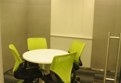 Small meeting room with a round white table and four bright lime green mesh chairs.