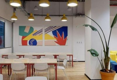 Light-filled workspace featuring wooden tables, white chairs, and a large abstract wall mural.