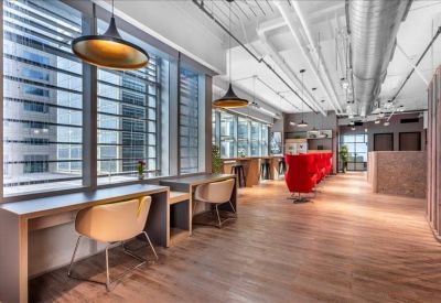 Coworking lounge with warm wooden floors, individual desk nooks, and vibrant red chairs.